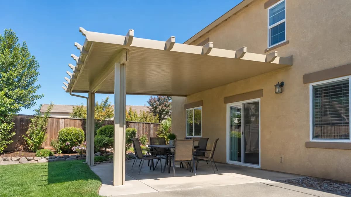 Sand-colored solid aluminum patio cover on a two-story tan stucco home shading a patio dining set